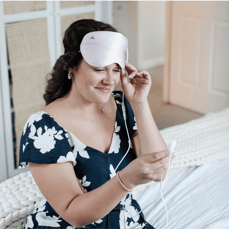 Woman adjusting Comfylids Heated Eye Mask SILK in pink while checking temperature controller.